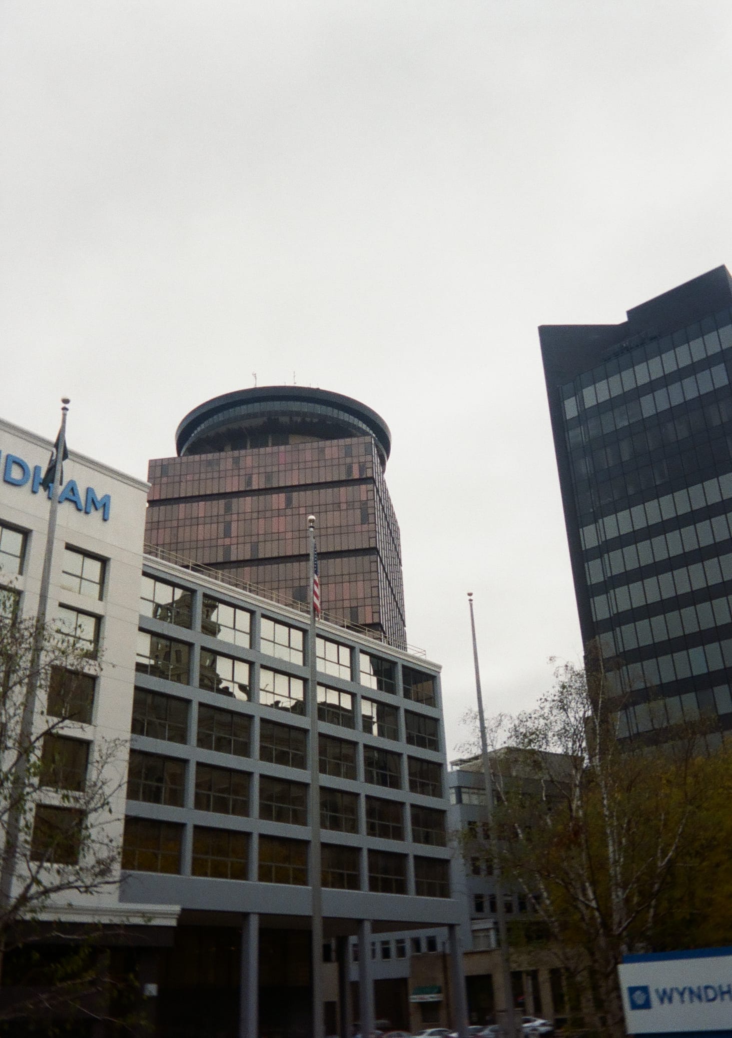 A copper colored glass building with a saucer shaped observation deck atop it behind a very boring looking Wyndham hotel