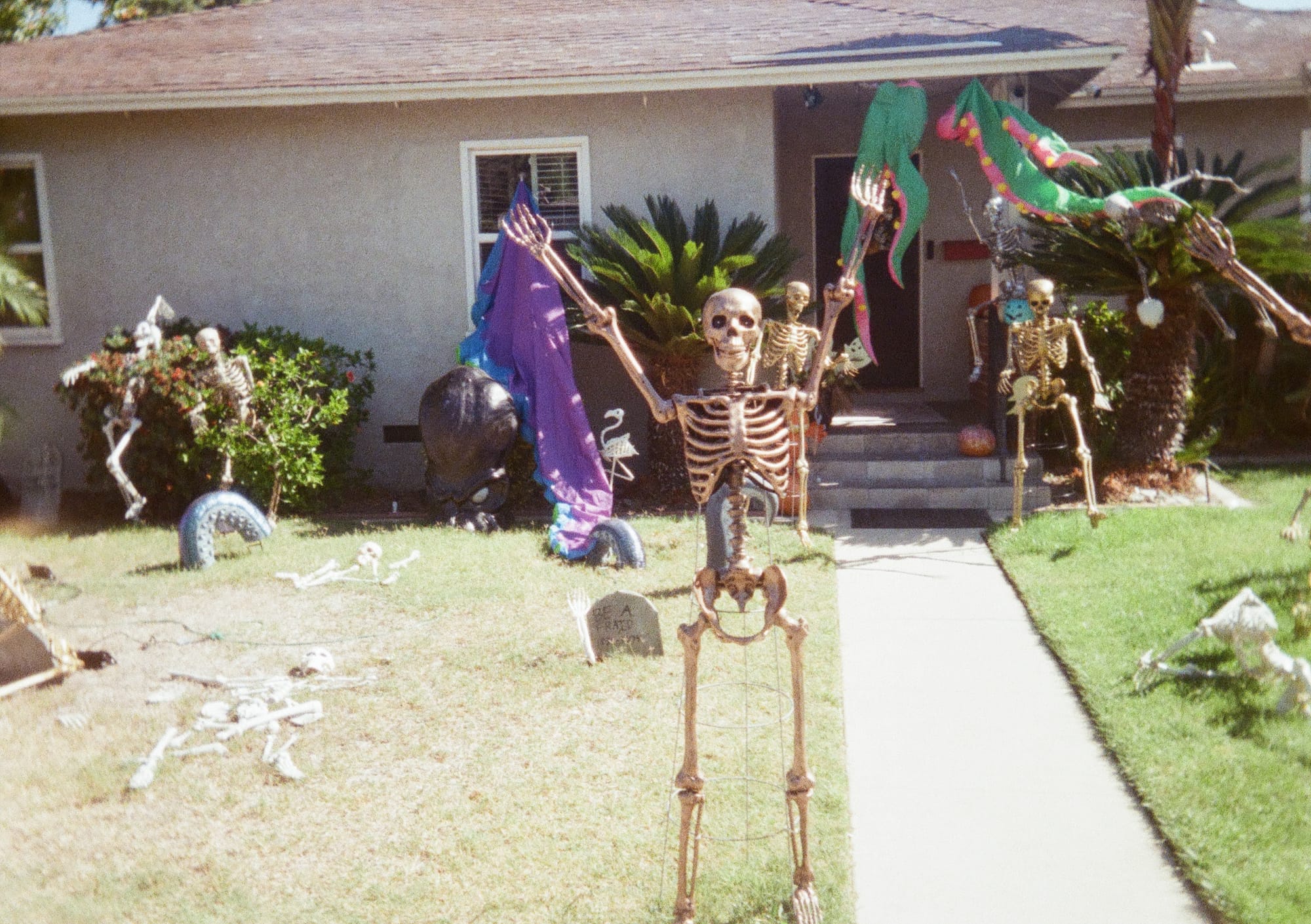 Gold painted skeletons doing jazz hands in front of a house