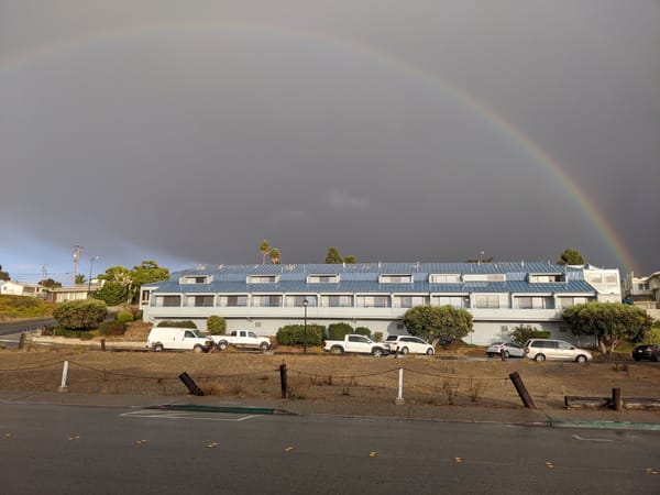 A rainbow against a grey sky above what looks like an apartment complex or hotel